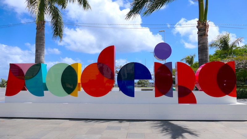 Buntes, großformatiges Madeira-Logo aus geometrischen Formen in Funchal vor blauem Himmel und Palmen.