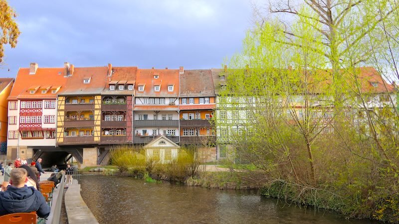 Die Krämerbrücke in Erfurt in ganzer Breite mit Weidenbäumen an der rechten Seite.